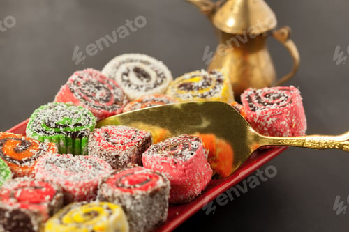 Preview: Colorful sweets on a red plate with a golden serving tool and a coffee pot nearby