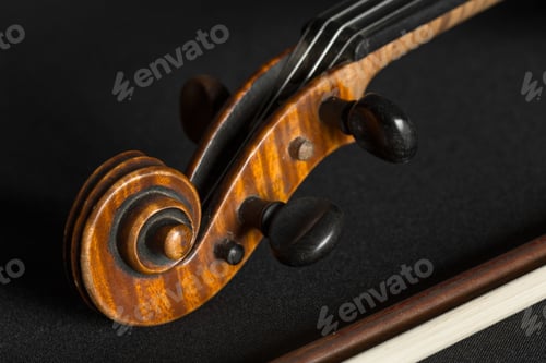 Preview: Close view of violin scroll and pegs on a dark surface with bow nearby