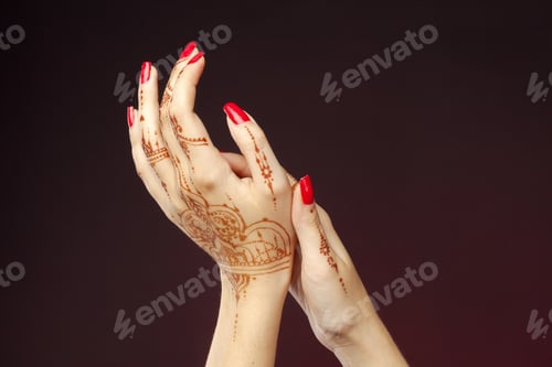 Preview: Hands with henna design and red nails in festive setting for celebration