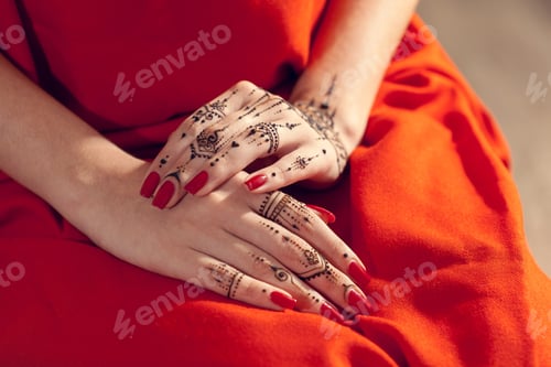 Preview: Hands with henna design resting on orange fabric before a celebration