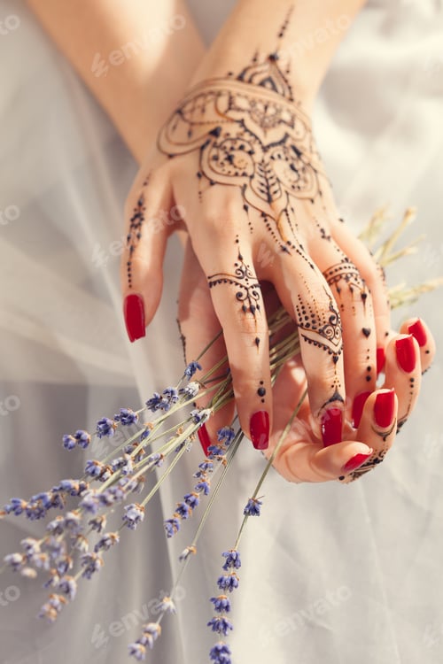 Preview: Hands with henna holding lavender flowers in soft light during a special event