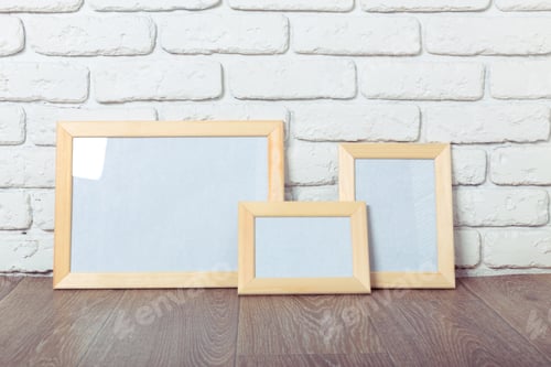 Preview: Frames sit on a wooden floor in front of a white brick wall during daylight