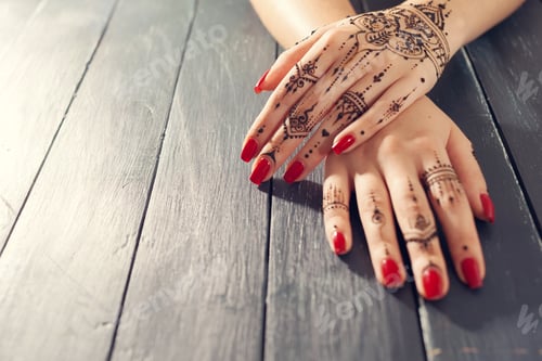 Preview: Hands with henna design and red nails on a wooden table