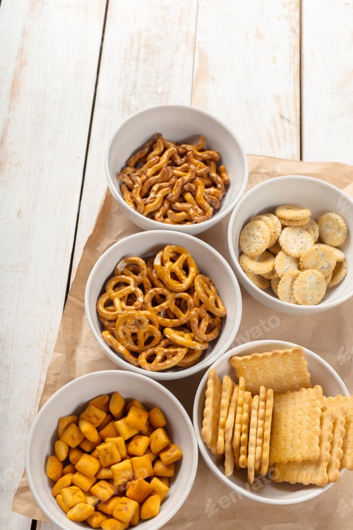 Preview: Snack bowls with various crunchy treats on a wooden surface during the daytime