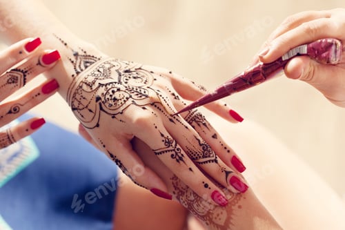 Preview: Henna application takes place on a hand with red nails during a sunny day at the beach