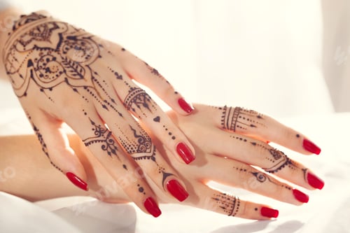 Preview: Henna designs on hands with red nails during a cultural event in a bright room