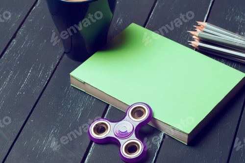 Preview: Fidget spinner, notebook, pencils, and a cup on a wooden table