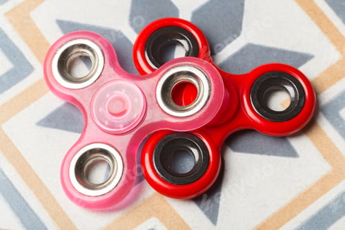 Preview: Two fidget spinners in pink and red colors resting on a patterned surface