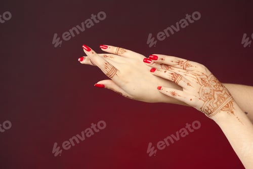Preview: Henna designs on hands with red nail polish during cultural celebration in closeup view