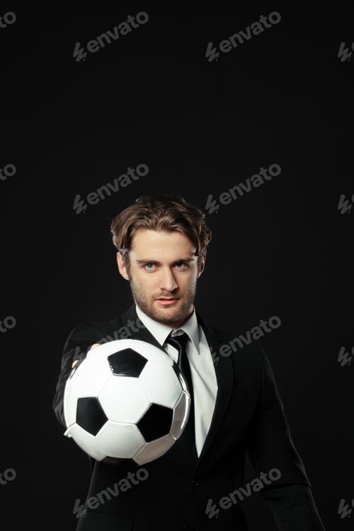 Preview: Man in suit holds soccer ball with confident look against dark background