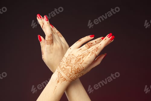 Preview: Hands with henna and red nails crossed in a creative pose in a dark background