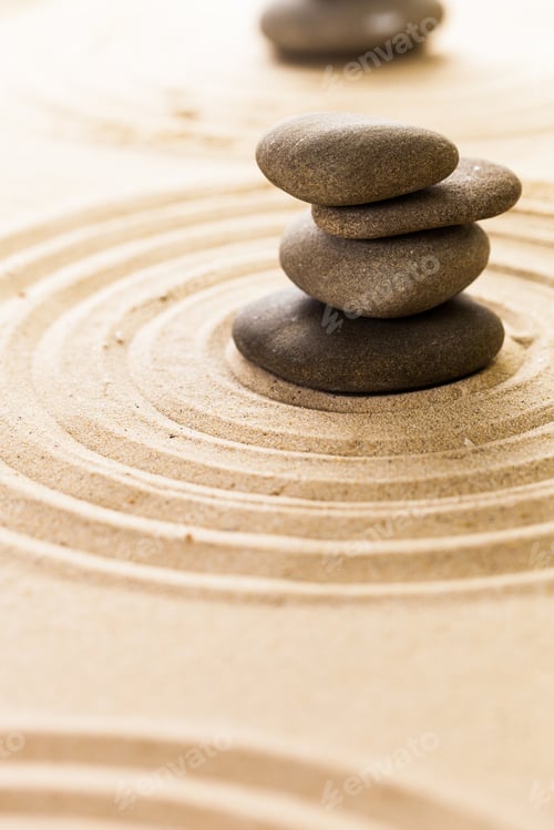 Preview: Balancing stones on sand create lines at a zen garden in daylight