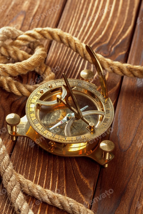 Preview: Old brass sundial sits on wooden table next to coiled rope during daylight hours