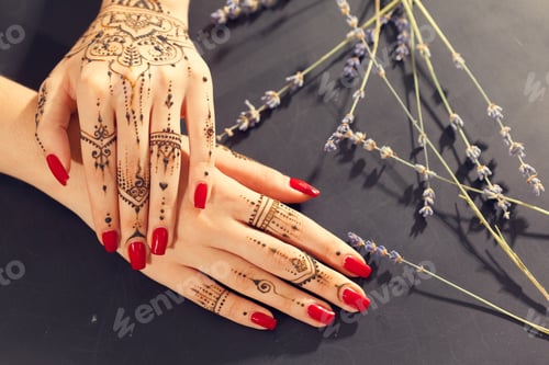 Preview: Hands with henna designs resting on black surface with lavender plants nearby in afternoon light
