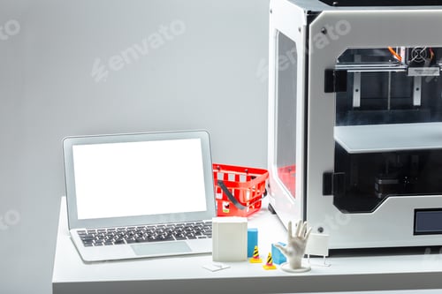 Preview: 3D printer works at a desk with a laptop and various small objects nearby
