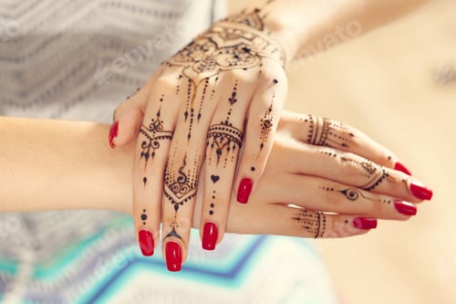Preview: Hands with henna design and red nails show art and culture in a light space during daytime