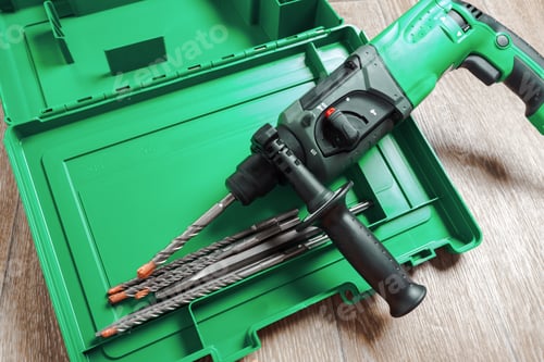 Preview: Electric drill and drill bits placed inside green toolbox on flat surface