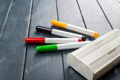 Preview: Markers in different colors on a wooden table with a white holder beside them