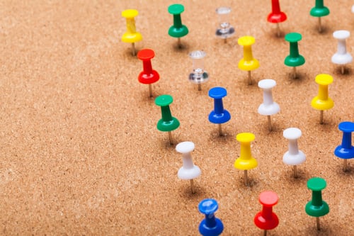 Preview: Colorful push pins arranged on a cork board showing various colors and shapes at an office setting