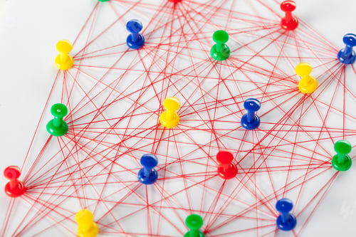 Preview: Colorful push pins and red strings create a network design on white paper in a workspace