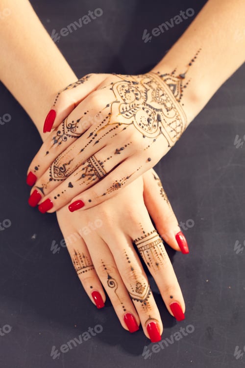 Preview: Hands with henna designs and red nail polish on a dark surface during a cultural event