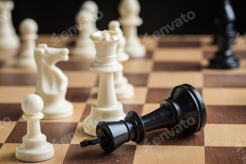 Preview: Close match in chess with fallen black king and white pieces on a wooden board