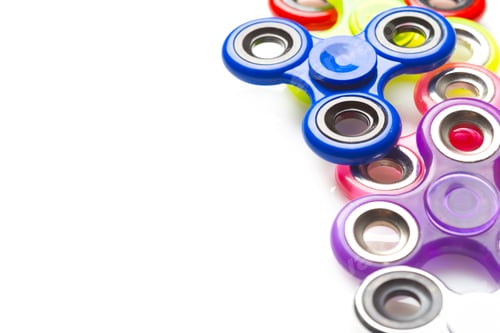 Preview: Fidget spinners of different colors arranged in a line on a white background