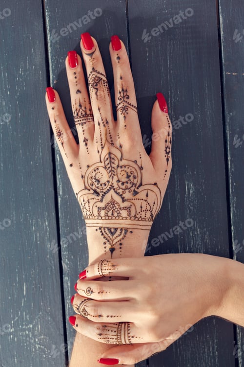 Preview: Art of henna tattoo on hands with red nails in natural light setting
