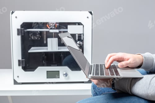 Preview: Person uses laptop to operate a 3D printer in a modern workspace setting