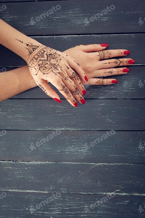 Preview: Hands with henna designs and red nail polish on a wooden surface during a cultural celebration