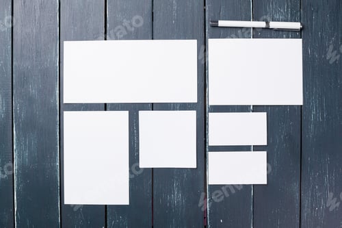 Preview: Various sheets of blank paper arranged on a grey wooden surface with a pen nearby