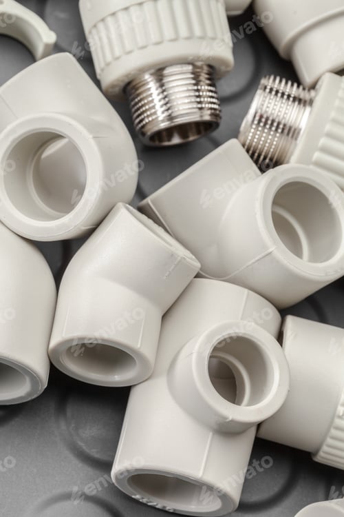 Preview: Collection of white plumbing fittings on a gray surface during midday