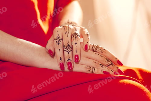 Preview: Hands with henna design rest on red dress while nails shine in bright color