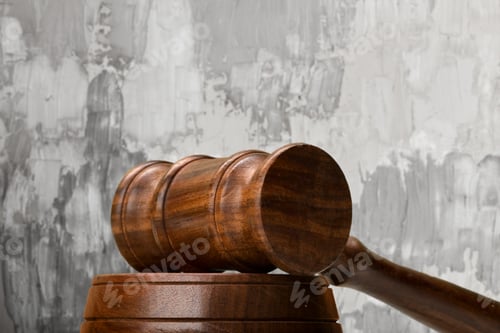 Preview: Wooden gavel rests on a round block on a gray wall background during a legal proceeding