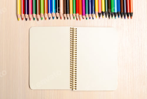 Preview: Colorful pencils and empty notebook on a wooden table ready for art and drawings
