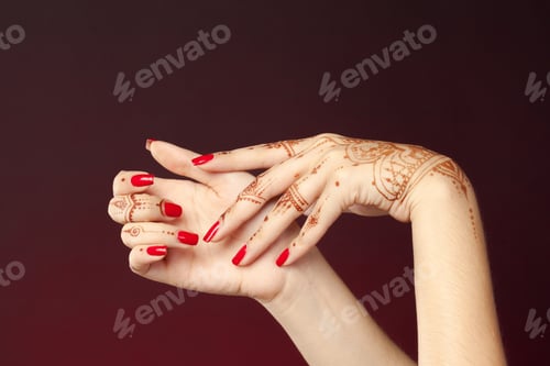 Preview: Hands with henna design and red nails hold each other in a creative display