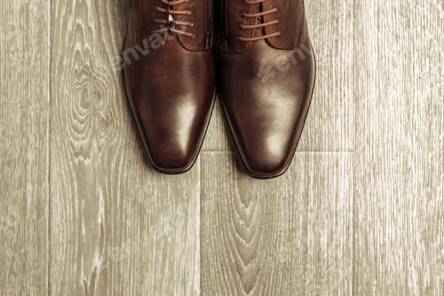 Preview: Brown leather shoes placed on floor with wooden texture in a simple setting during daylight