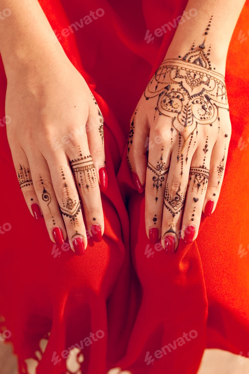 Preview: Hands decorated with henna designs resting on a bright red fabric during a cultural event