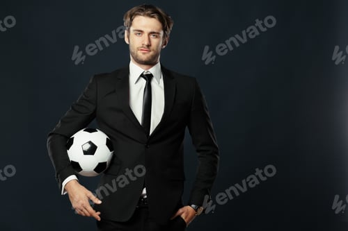 Preview: Man in a suit holds a soccer ball in a studio setting with a dark background