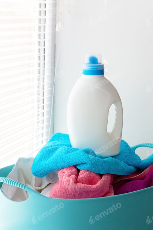 Preview: Laundry basket with colorful towels and detergent placed near a window during the day