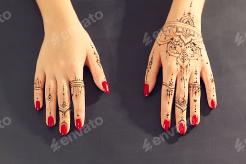 Preview: Hands with henna designs and red nail polish on a flat surface in a bright room