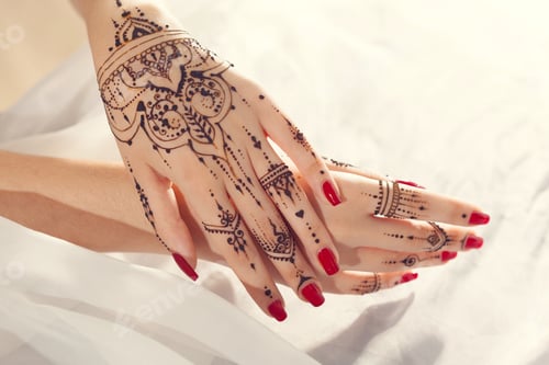 Preview: Hands with henna designs and red nails resting on a light surface in a bright room