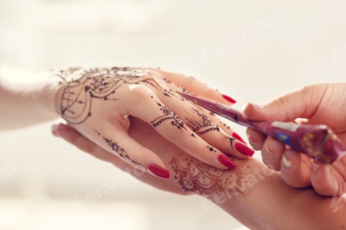 Preview: Woman receives henna art on hand during celebration at a cultural event in a bright setting