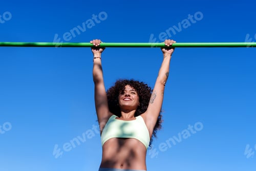Preview: Woman exercising outdoors, hanging on a pull up bar, feeling strong and enjoying her workout