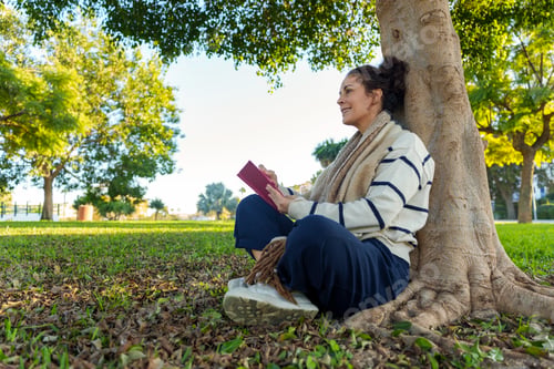 Preview: Woman enjoying quiet time reading a book under a large tree in a sunny park, finding peace and relax