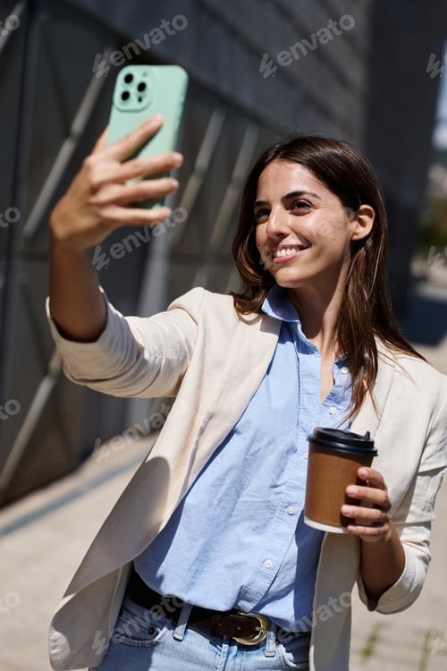 Preview: Woman smiling taking selfie holding coffee in city