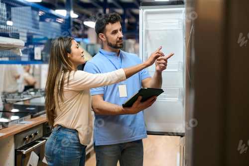 Preview: Shop assistant explaining refrigerator features to customer