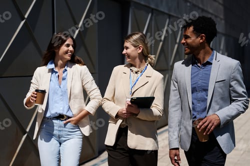 Preview: Business colleagues walking outdoors smiling drinking coffee