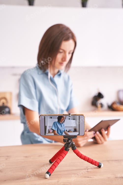 Preview: Young woman record video at kitchen. Self portrait. Blogger selfie video