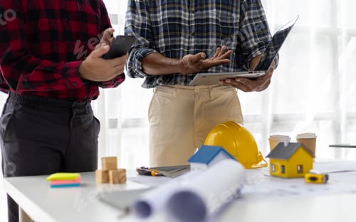 Preview: Construction contractor holding laptop discussing construction plan according to architect's design.